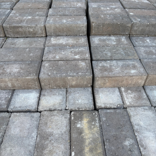 Close-up of a cobblestone pathway with a mix of dark and light gray stones. The uneven texture and slight gaps suggest a rustic, weathered look.