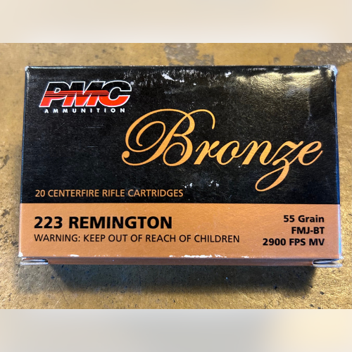 A box of PMC Bronze ammunition sits on a wooden surface. The label reads 