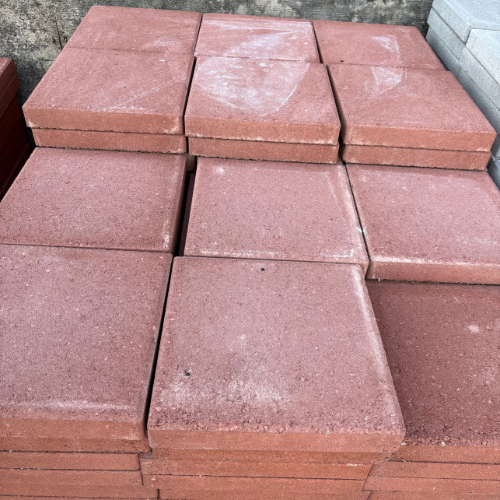 A stack of red paving stones is neatly arranged, showing uniformity and texture. The surface appears slightly dusty, indicating outdoor storage.