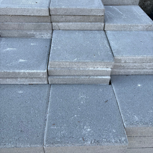 Stacks of gray concrete paving slabs arranged in a neat, symmetrical pattern. The slabs exhibit a rough texture and weathered appearance.