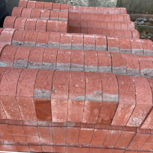 Stack of neatly arranged red bricks, showing some wear and discoloration, creating a repetitive pattern against a concrete backdrop.