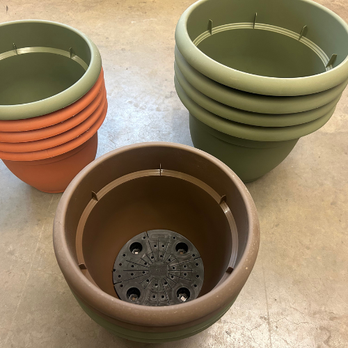 A collection of stacked plastic pots in green, terracotta, and brown hues on a concrete floor. The scene feels calm and organized.