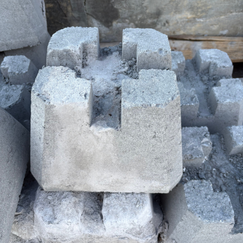 A stack of interlocking concrete blocks is shown, with rough textures and a light gray color. The scene conveys construction or industrial use.