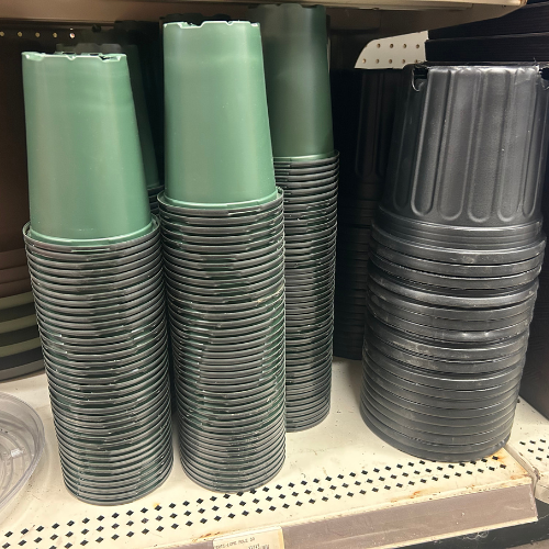 Stacks of green and black plastic plant pots are arranged neatly on a store shelf. The scene conveys an organized and utilitarian tone.