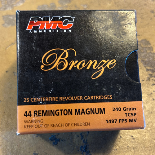 Box of PMC Bronze .44 Remington Magnum cartridges on a textured surface, labeled with 240 grain, TCSP, 1497 FPS MV, and a safety warning.