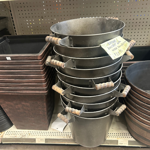 Stacked vintage metal buckets with wooden handles on a store shelf. A note says 