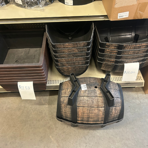 Stacked wooden barrel-style planters and rectangular planters on a store shelf. Prices are displayed on white tags: $12.50 and $25.00.