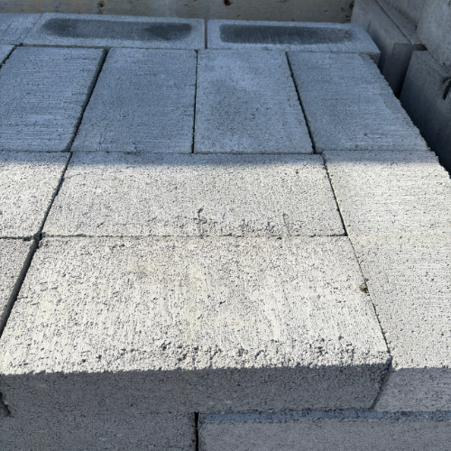 Stacked gray concrete bricks arranged neatly against a concrete wall, casting soft shadows. The scene conveys a sense of order and stability.