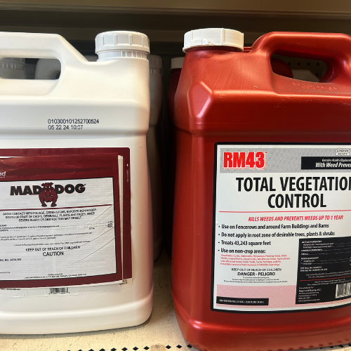 Two large herbicide containers sit side by side on a shelf. The left is white with a 