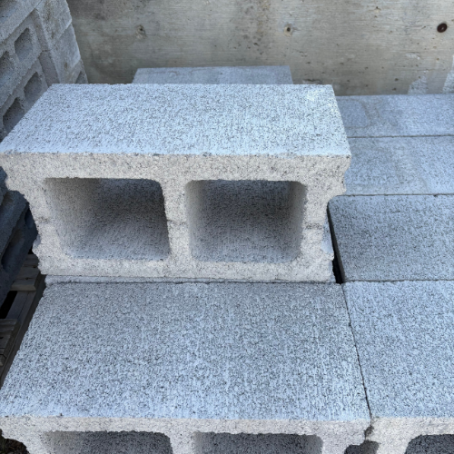 Stacked gray concrete cinder blocks, each with two rectangular holes, are arranged neatly on a construction site, conveying an industrial tone.