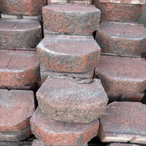 Stacked hexagonal paving stones in shades of brown and gray, showcasing a rough texture. The arrangement is orderly, suggesting construction preparation.