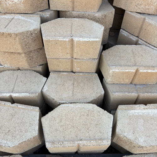 A stack of interlocking concrete pavers in a tan color, arranged in rows. The texture appears rough, evoking a sense of durability and functionality.